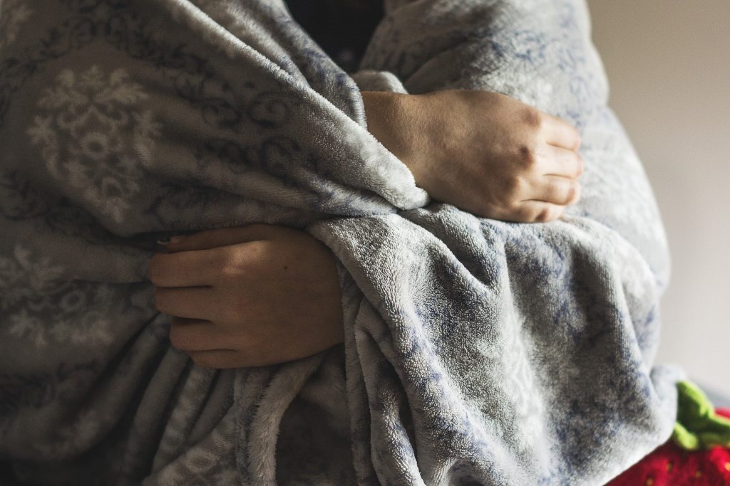 A person drawing a blanket close to them because they are cold.